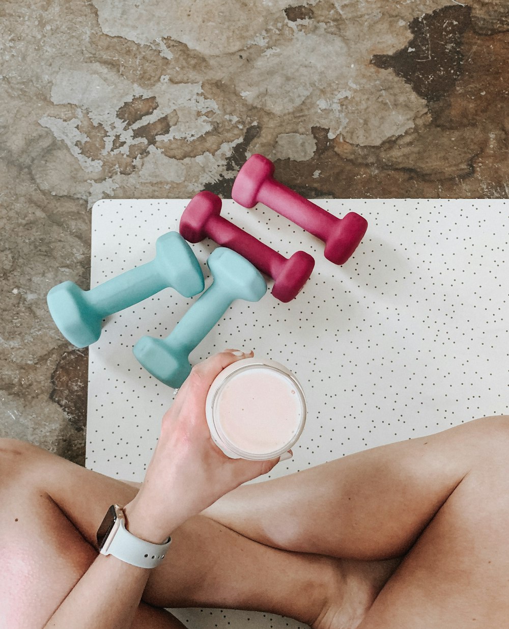 person holding white liquid filled cup above two pairs of dumbbells