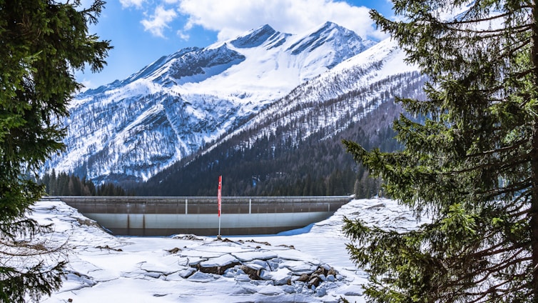A striking high-contrast image of a sleek hydroelectric dam nestled within a rugged mountain landscape under a dramatic sky.