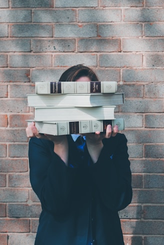 person holding pile of books near face