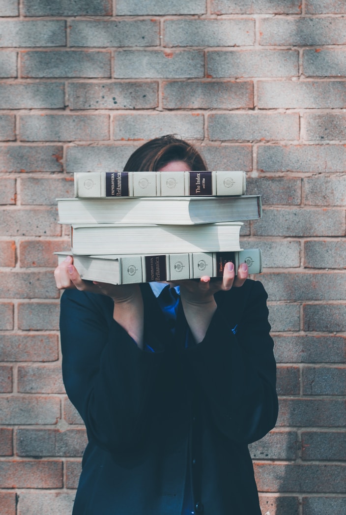 person holding pile of books near face