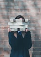 person holding pile of books near face