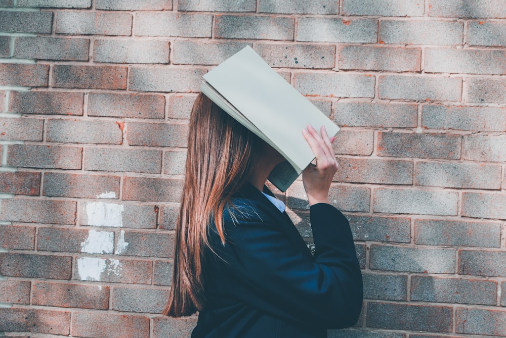 Frau bedeckt ihr Gesicht mit einem aufgeschlagenen Buch