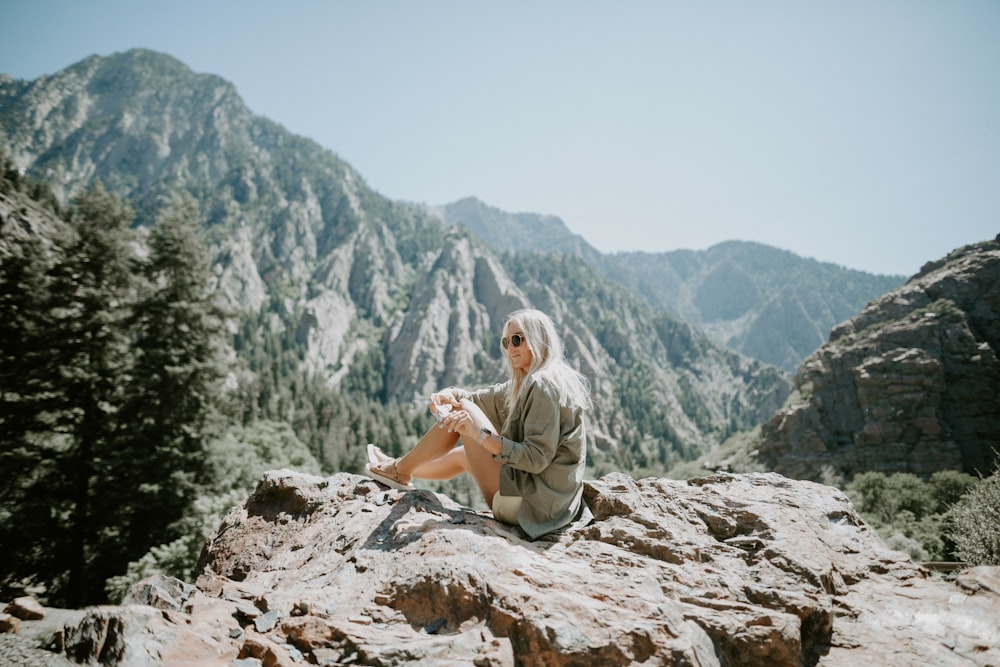 Mujer sentada en la montaña de observación de la colina rocosa bajo cielos azules