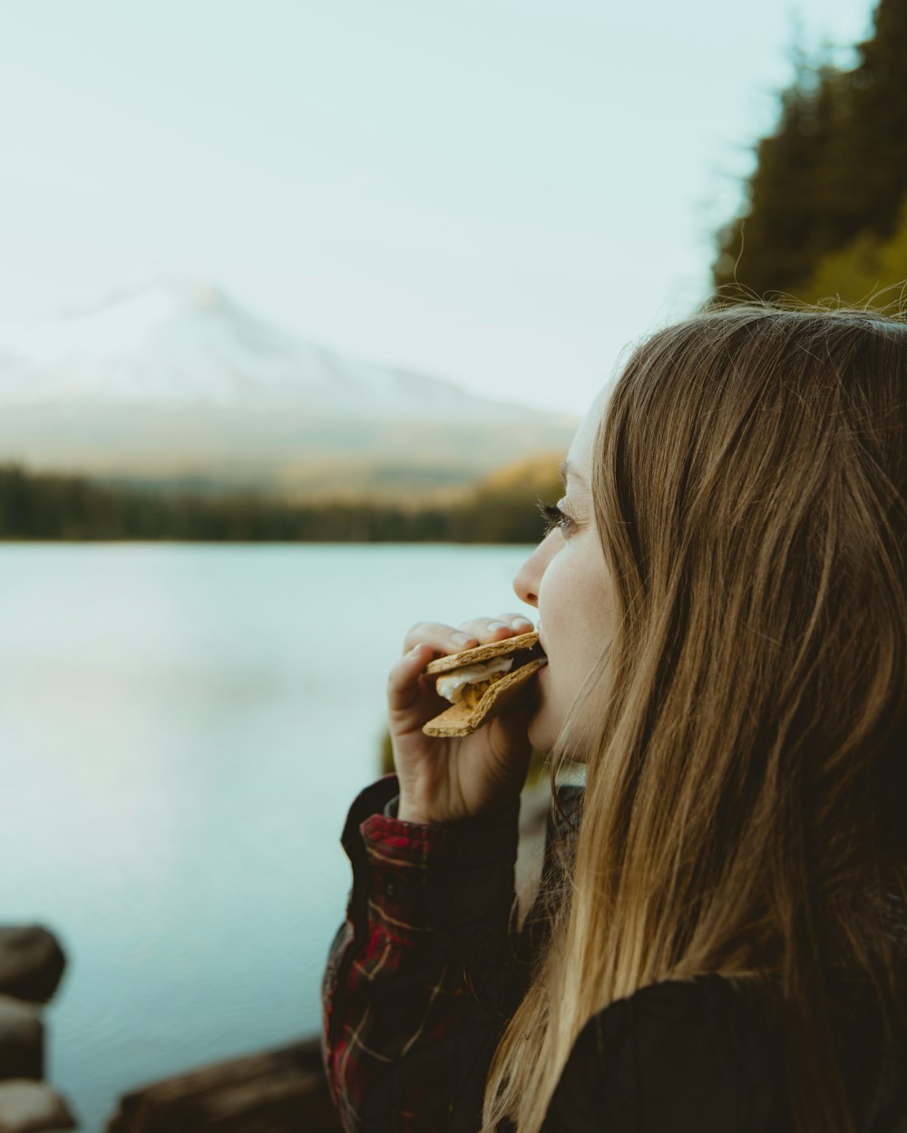 Donna in piedi e che mangia cibo di fronte allo specchio d'acqua che osserva la montagna