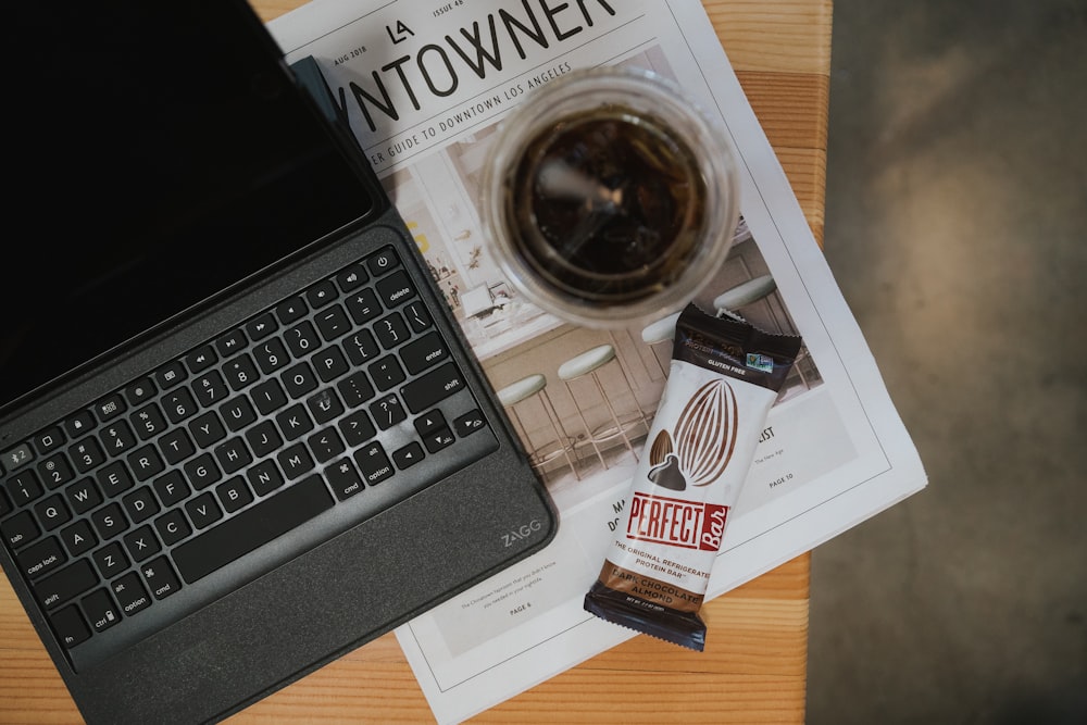 컵 근처에 키보드가 있는 회색 태블릿 컴퓨터와 테이블 위의 초콜릿 팩