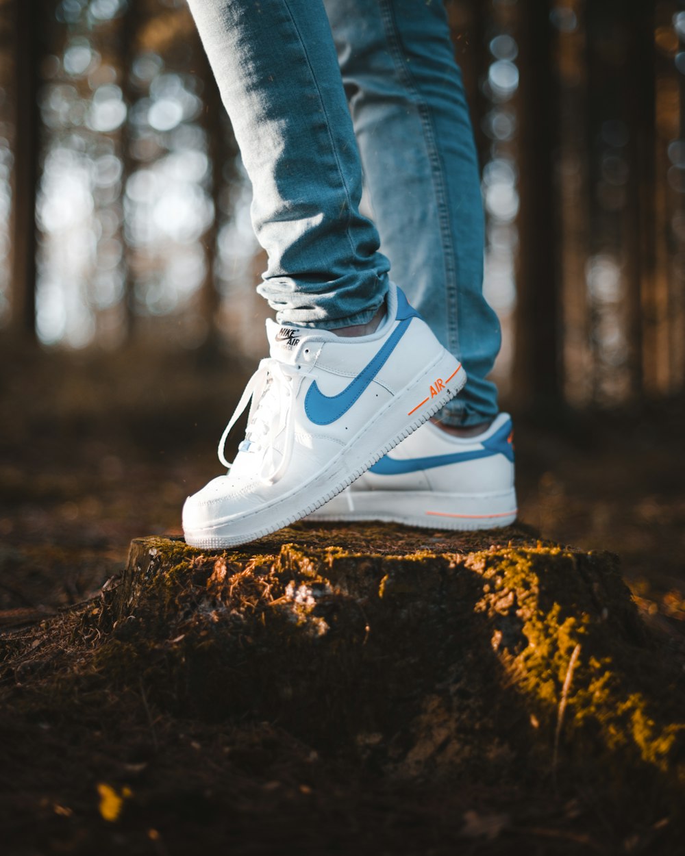 person wearing blue denim jeans and white Nike Air Max shoes standing on tree stomp