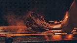Rounded photo of a sizzling steak on the grill with flames around.