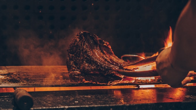 Close-up of a sizzling Argentine bife ancho steak on a grill with smoke rising.