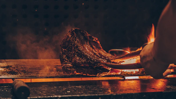 Close-up of a premium cut of steak sizzling on a grill with golden flames.