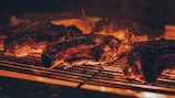 Close-up of sizzling alpaca meat grilling over glowing embers in a rustic setting.