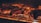 Several pieces of meat are being grilled over an open flame. The surface of the meat is charred, indicating high heat and searing. The glowing embers and fiery orange hue create a warm atmosphere.