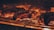 Several pieces of meat are being grilled over an open flame. The surface of the meat is charred, indicating high heat and searing. The glowing embers and fiery orange hue create a warm atmosphere.