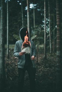 man holding burning paper near trees