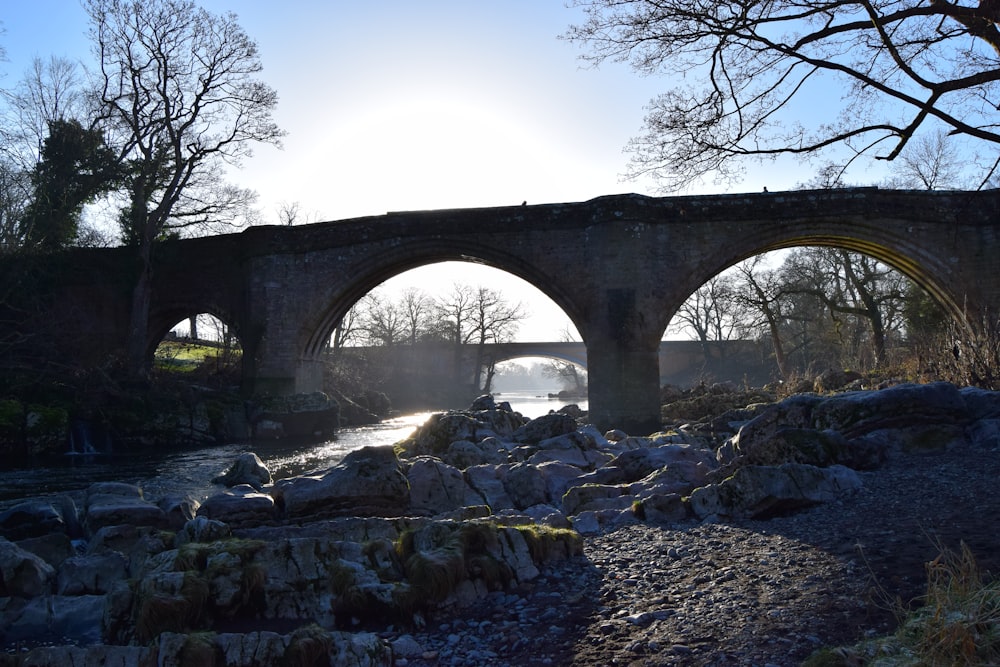 rock formations near flowing stream viewing bridge beside bare trees under blue and white skies