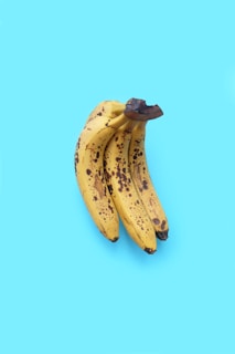 Three ripe bananas with brown spots on the peel are set against a bright blue background.