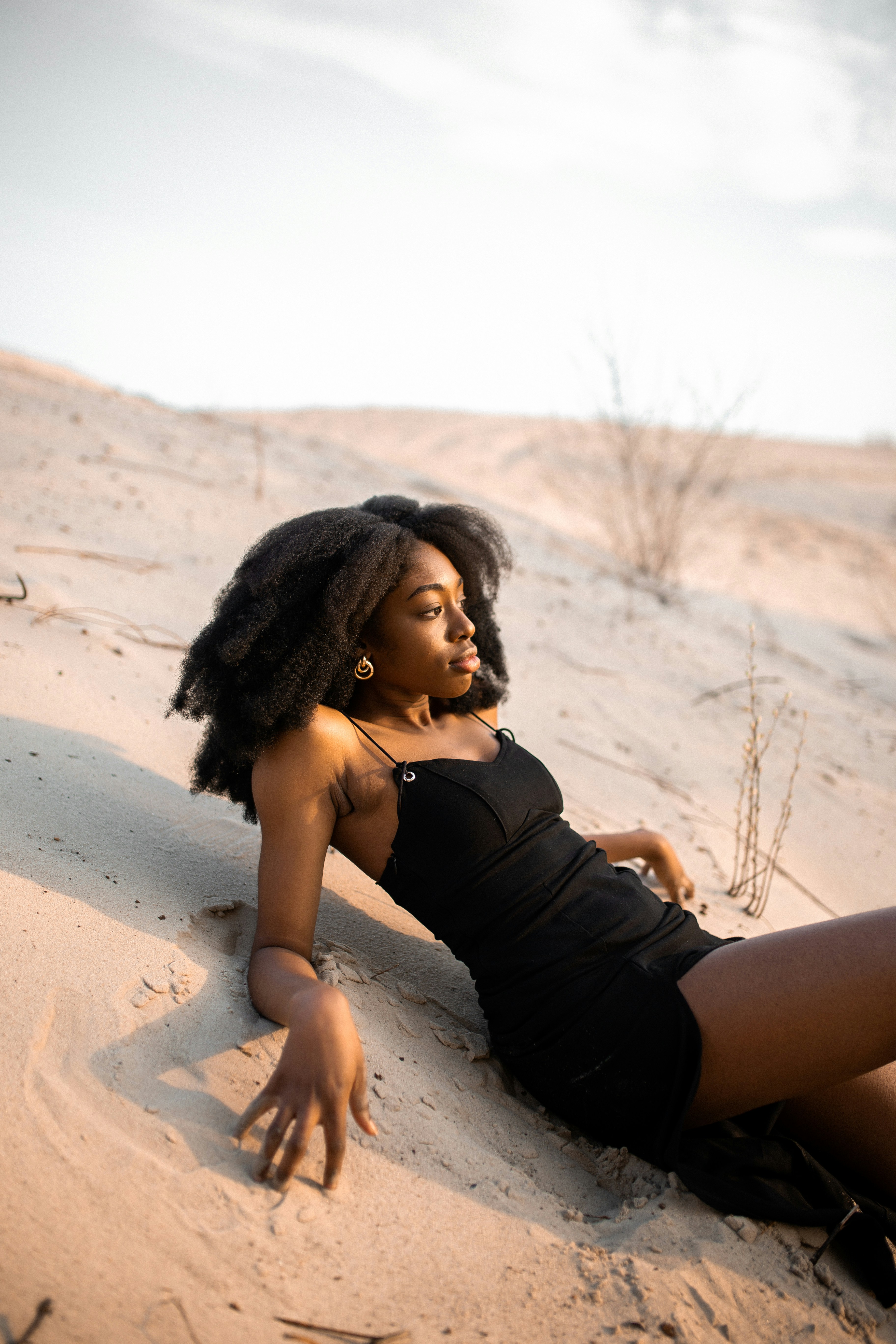 woman in black dress leaning on sand during daytime