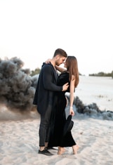 a man and a woman standing on top of a sandy beach