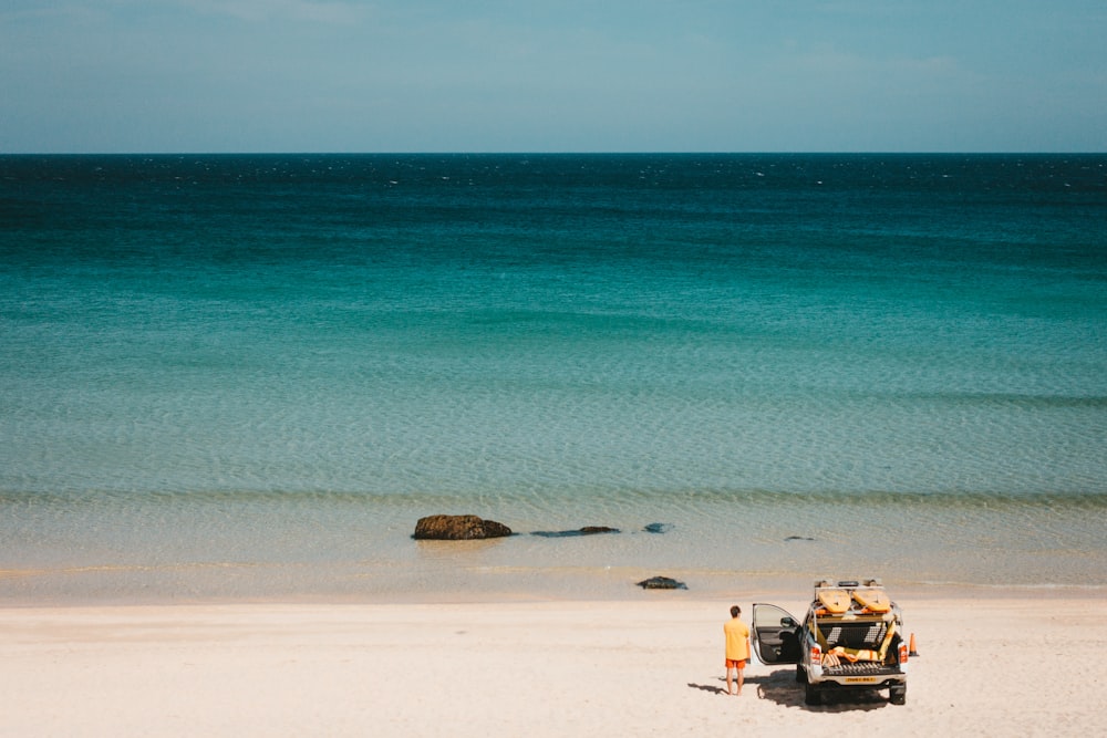 man standing near vehicle beside seashore viewing calm sea