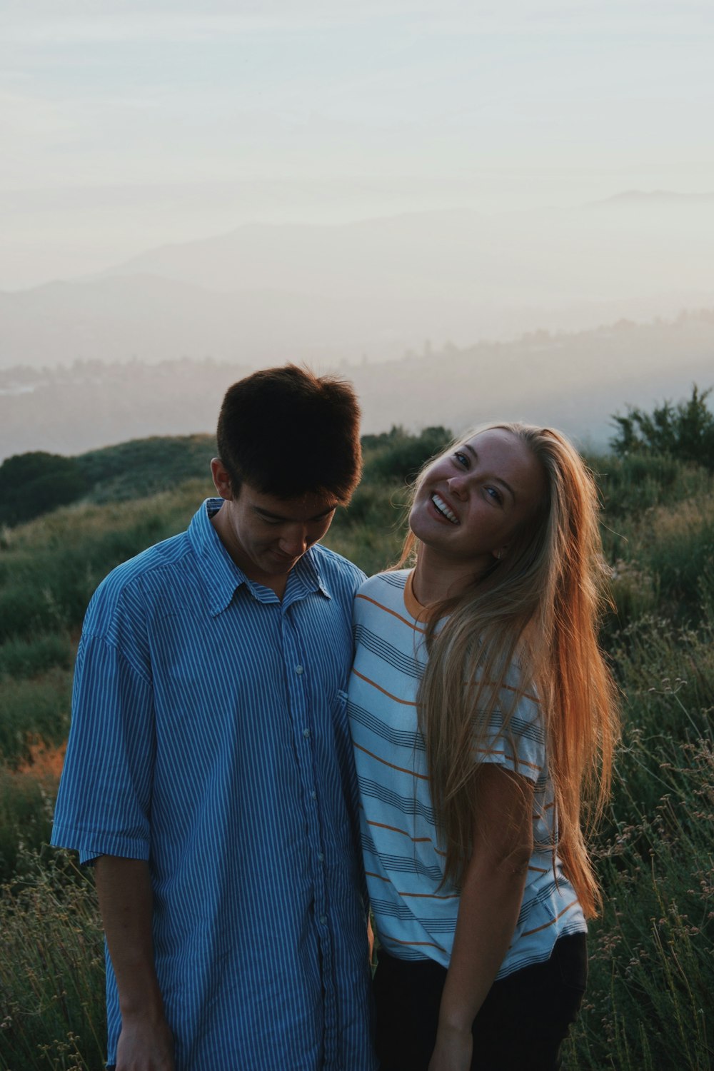 man wearing blue dress shirt and woman wearing white and gray stripe shirt standing on grassland