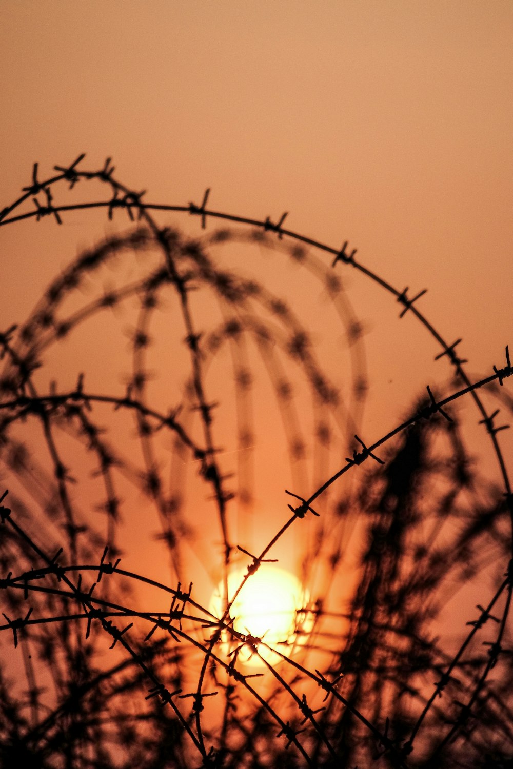 the sun is setting behind a barbed wire fence
