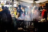 A vibrant street food stall serving sate maranggi with smoke rising from the grill