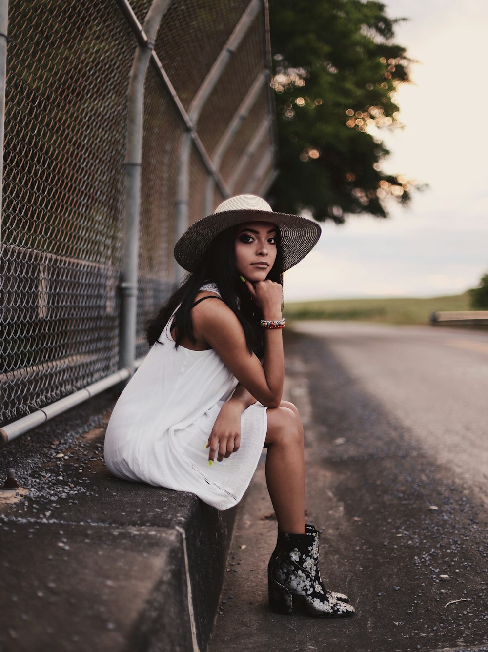 woman wearing white sleeveless dress sitting besides gray cyclone fence