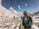 Several mountaineers are trekking through a snowy mountainous landscape. The scene features high, snow-capped peaks under a clear blue sky. The climbers are dressed in winter gear, with backpacks and protective outerwear. Snowflakes can be seen in the air, adding to the cold and adventurous atmosphere.