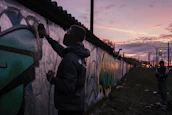 Painter carefully applying color to the exterior wall of a residential building at sunset.