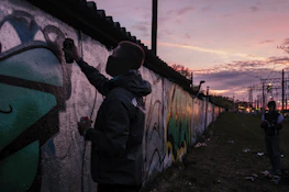 Painter carefully applying color to the exterior wall of a residential building at sunset.