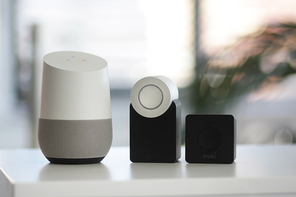 weißer und grauer Google Smart Speaker und zwei schwarze Lautsprecher