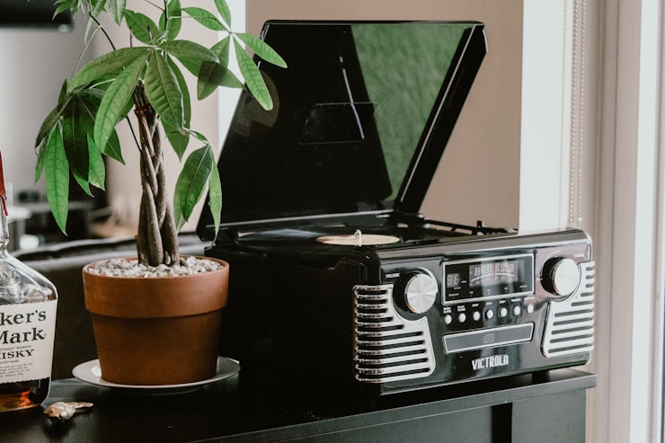 Black retro record player by Victrola next to green plant on black desk in living room.