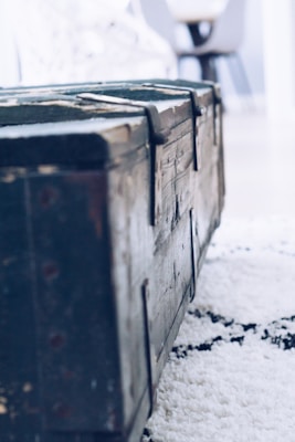 A rustic wooden storage chest with visible grain and metal accents, placed at the foot of a bed.