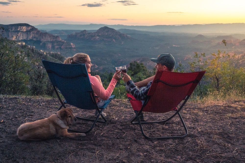 duas pessoas sentadas em cadeiras de acampamento enquanto observam a montanha