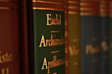Close-up view of a row of books with green and brown spines, featuring gold lettering with names like Euclid, Archimedes, and Apollonius.