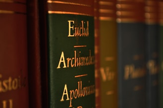 Close-up view of a row of books with green and brown spines, featuring gold lettering with names like Euclid, Archimedes, and Apollonius.