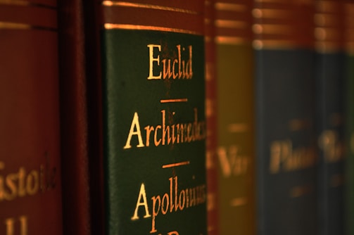 Close-up view of a row of books with green and brown spines, featuring gold lettering with names like Euclid, Archimedes, and Apollonius.