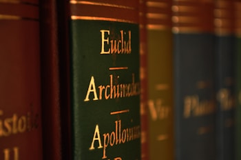 Close-up view of a row of books with green and brown spines, featuring gold lettering with names like Euclid, Archimedes, and Apollonius.
