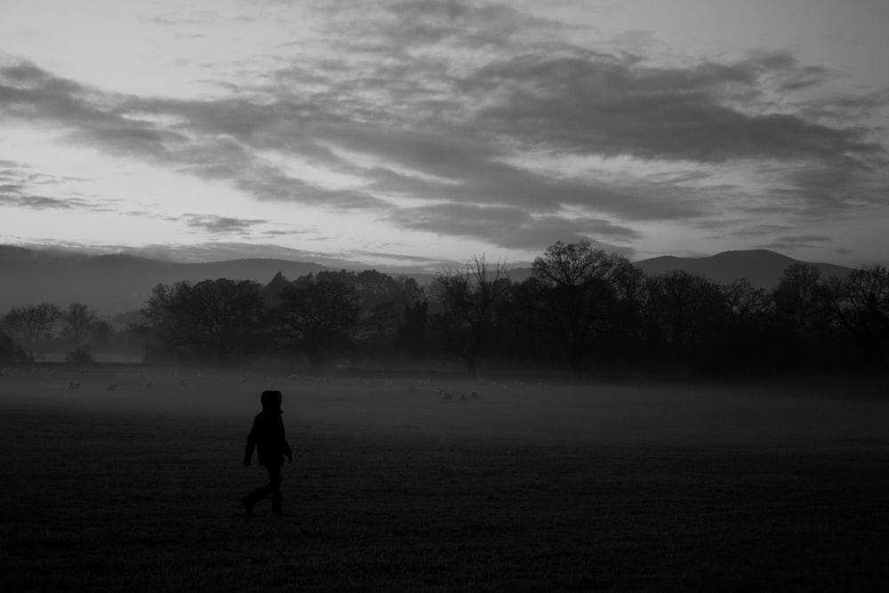 grayscale photo of person walking in the middle of forest