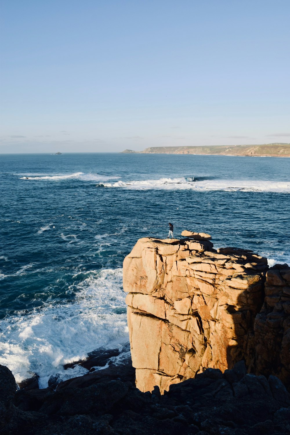 person standing on rock cliff beside body of water