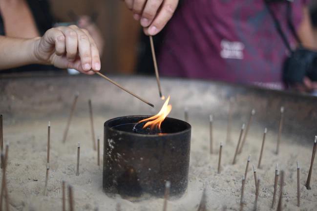 Close-up of a hand lighting a copal incense stick surrounded by soft candlelight.