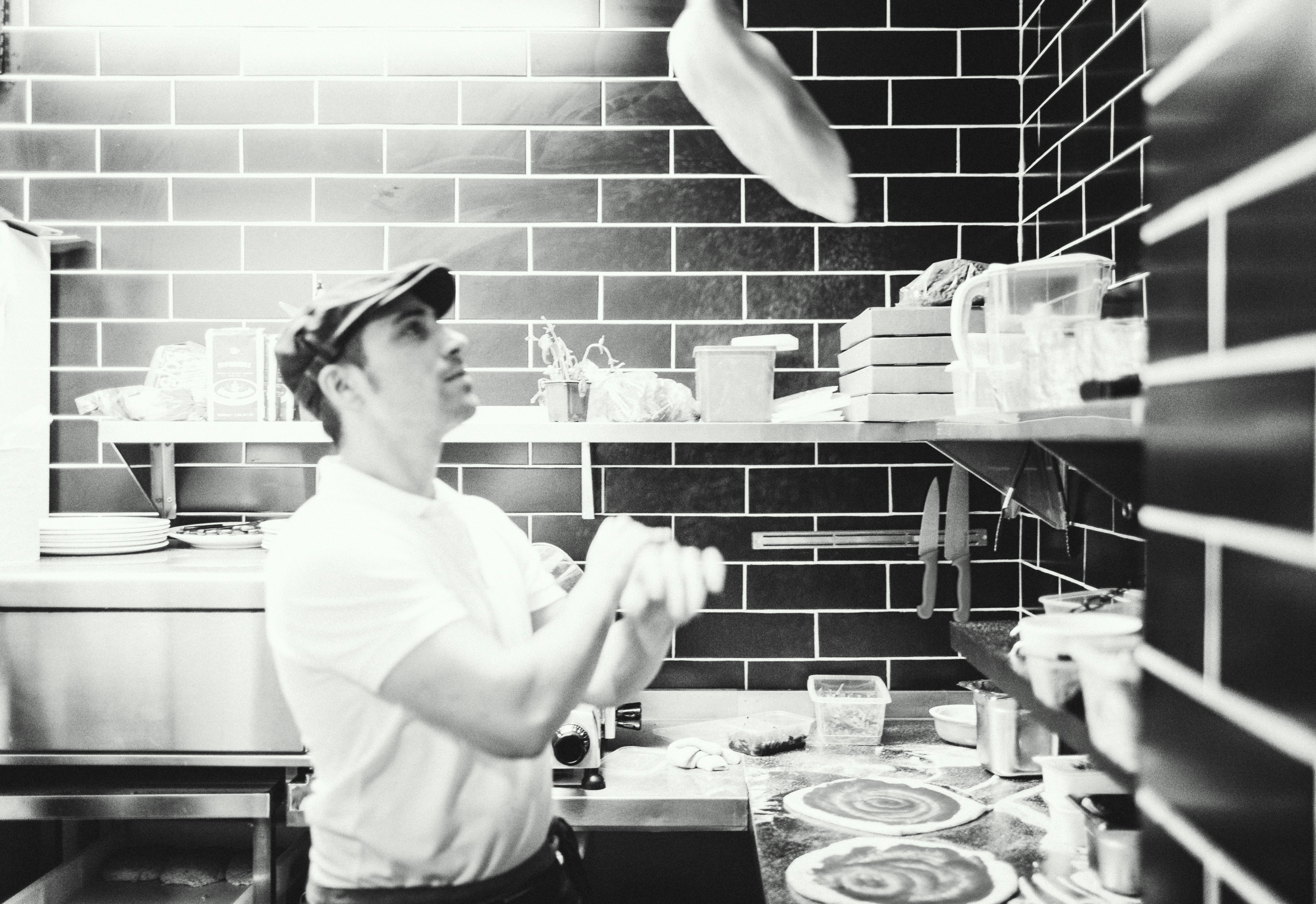 Pizza chef stretching dough in a dark professional kitchen with warm amber lighting