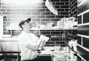 A pizza chef tossing dough in the air inside a lively kitchen.