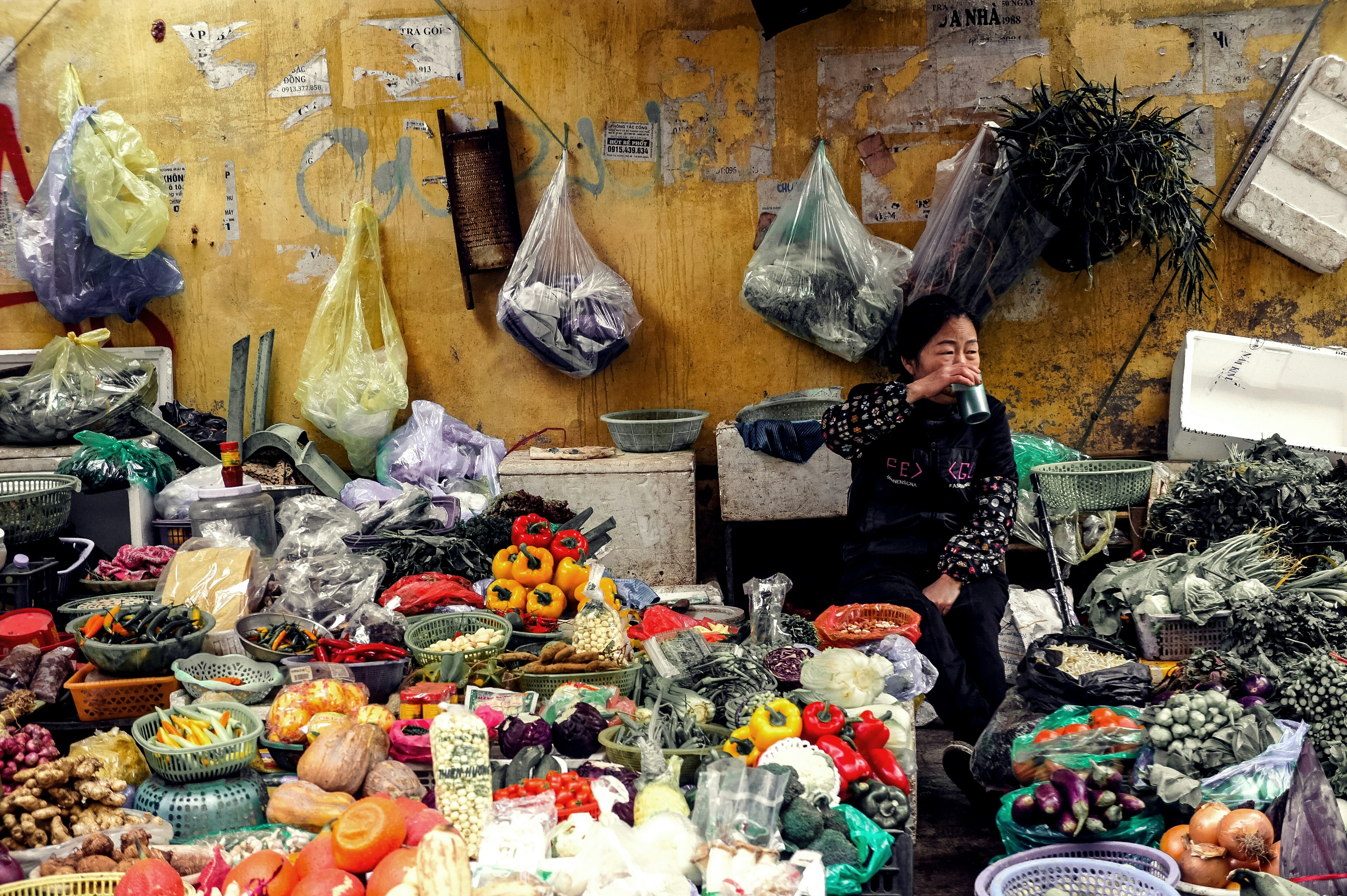 woman drinking cup sitting among vegetable display