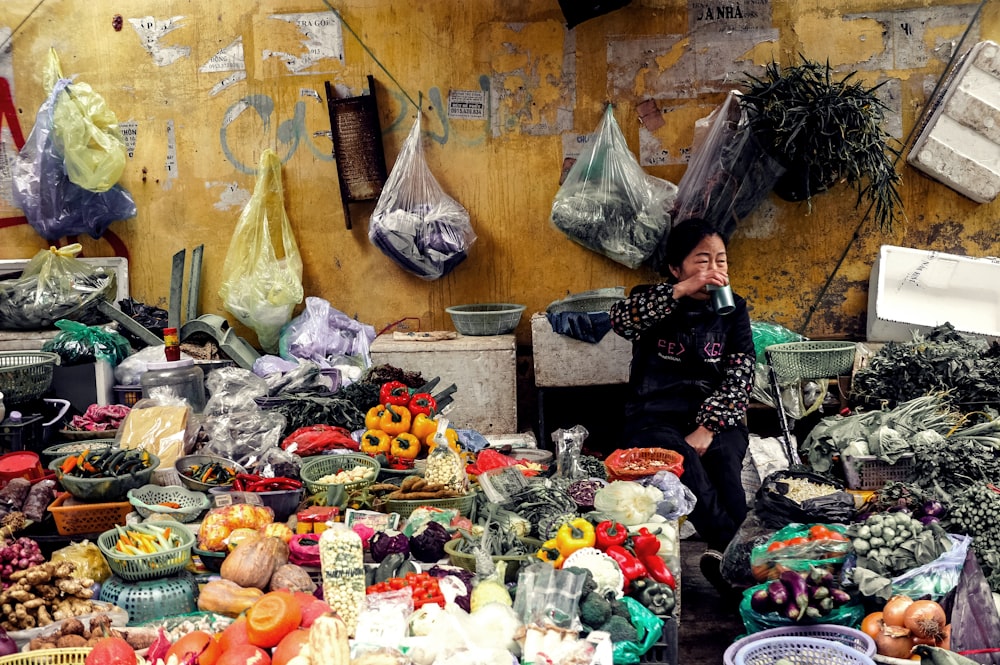 woman drinking cup sitting among vegetable display