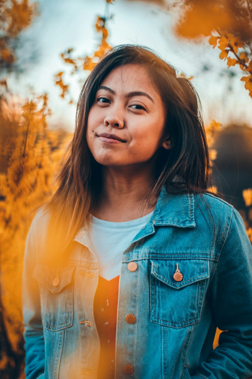 woman smirking wearing denim button-up jacket near leaves