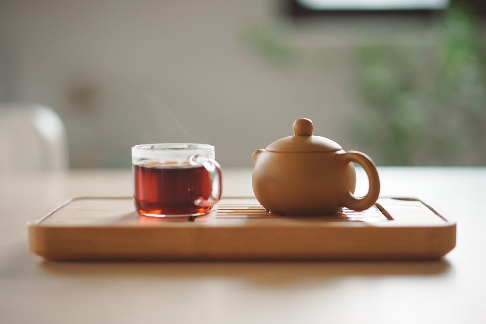 taza de vidrio transparente con té cerca de la tetera de cerámica marrón