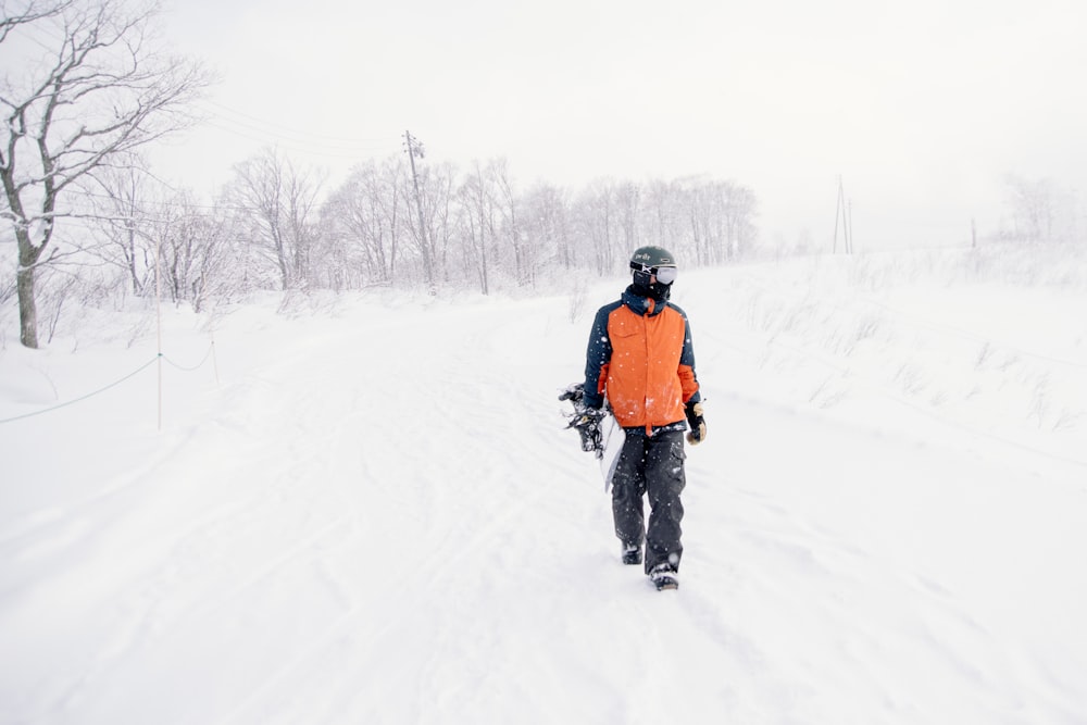 person in orange and black outfit holding snowboard