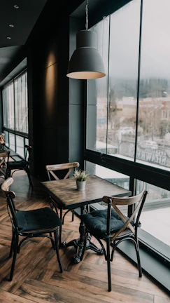 A sunlit corner of a rustic coffee shop with wooden tables and potted plants.