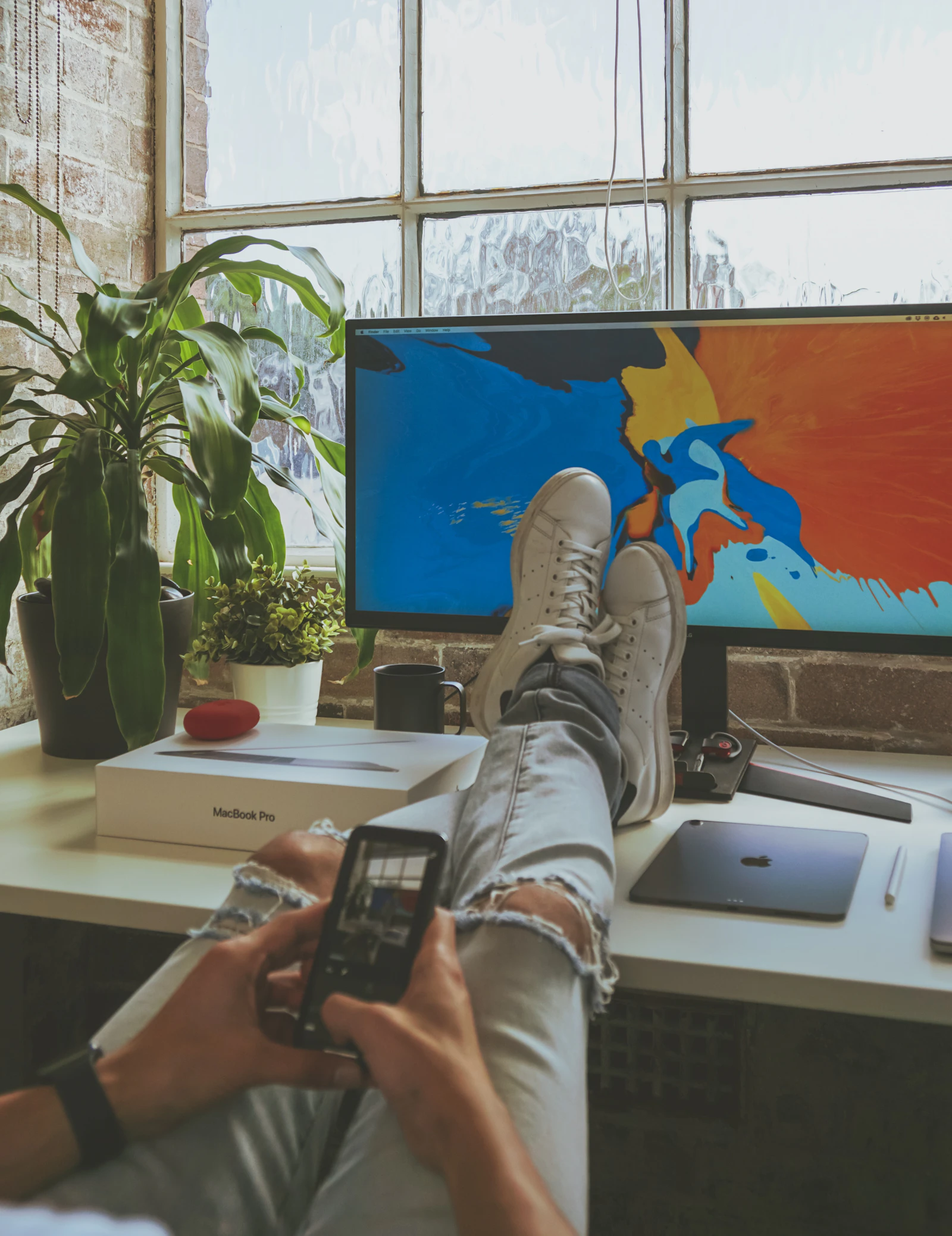 Person using smartphone while resting both feet on computer desk
