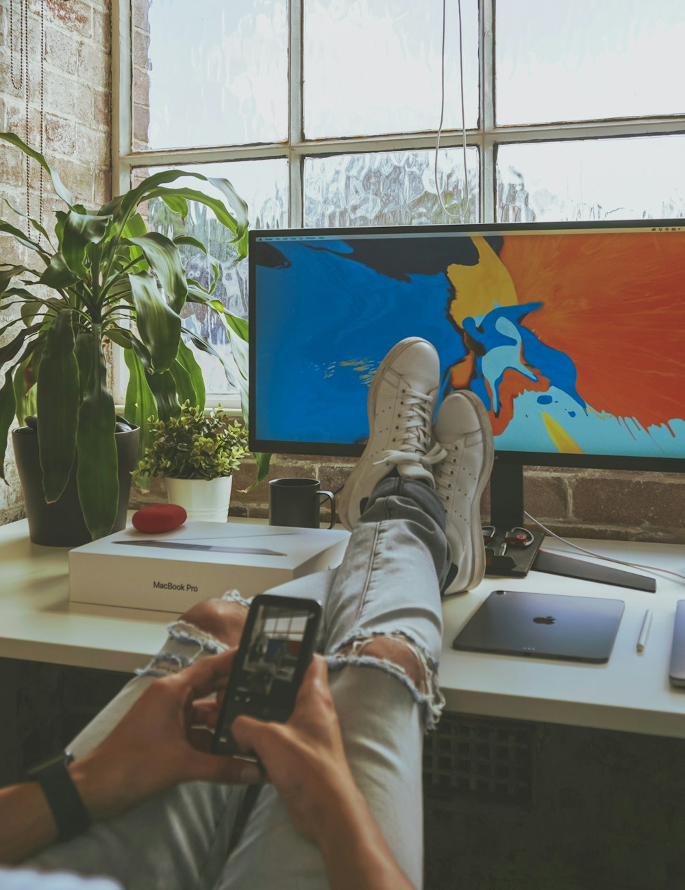 person using smartphone while resting both feet on computer desk